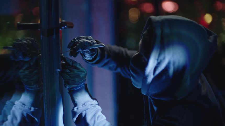 A person wearing a hoodie and gloves engaged in an illicit activity such as breaking into a building at night
