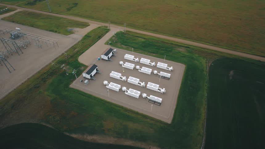 Aerial view of a cluster of white rectangular structures neatly aligned on a plot of land surrounded by grass