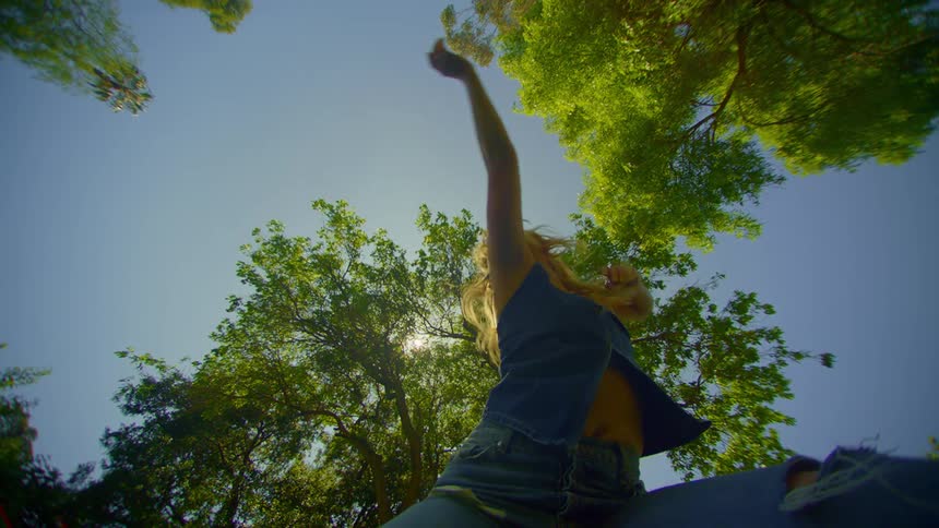 A woman wearing jeans a an open shirt dances near trees
