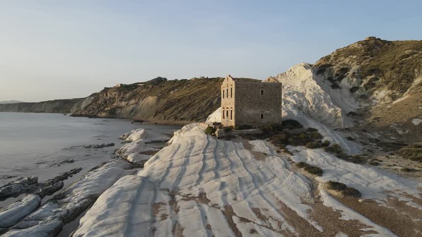 Abandoned stone structure on a white earthen hill with the sea in the background and a clear sky