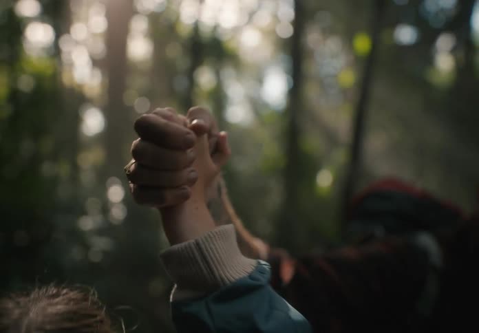 Parent holds hands with daughter as they hike through the forest on a sunny day