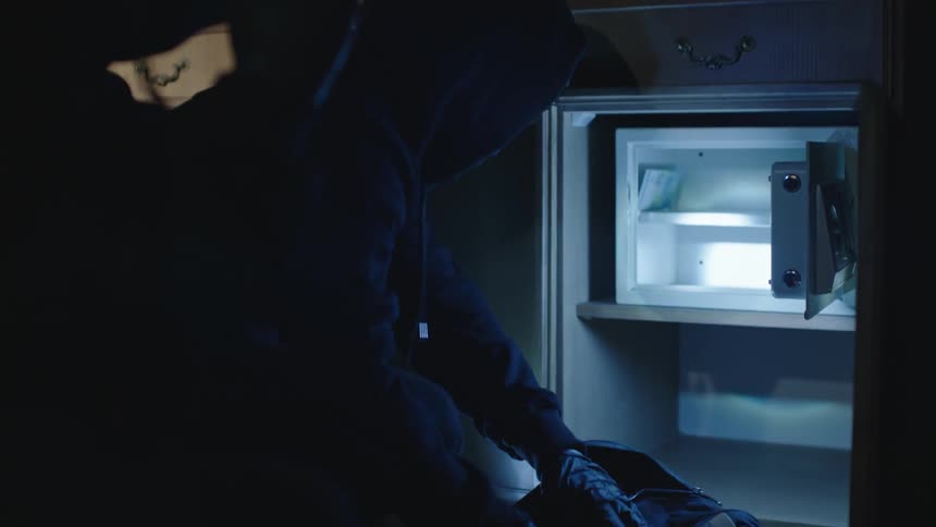 Thief steals money from a safe in a dark room