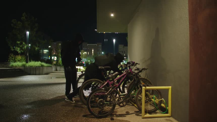 Two people wearing hoodies come to a bicycle parking take out a large wirecutter and steal two bicycles