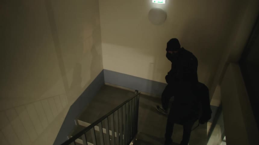 Two people wearing hoodies and masks engaged in an illicit activity such as breaking into a building at night