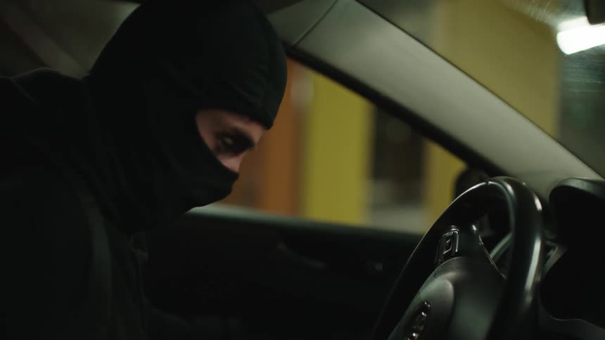 A masked person breaks into a car that is parked in a parking garage