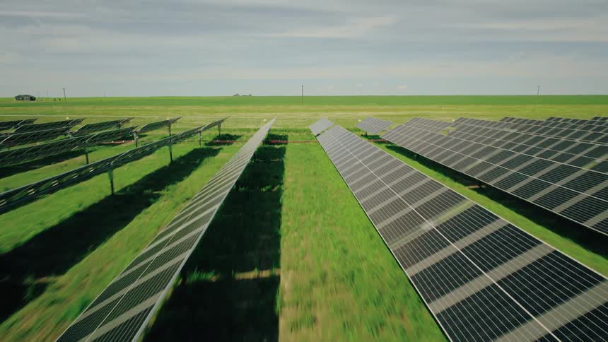 Flying through rows of solar panels in a field in a rural area