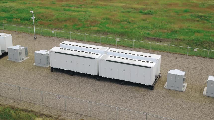 An aerial view of a fenced area with large electrical infrastructure and transformers