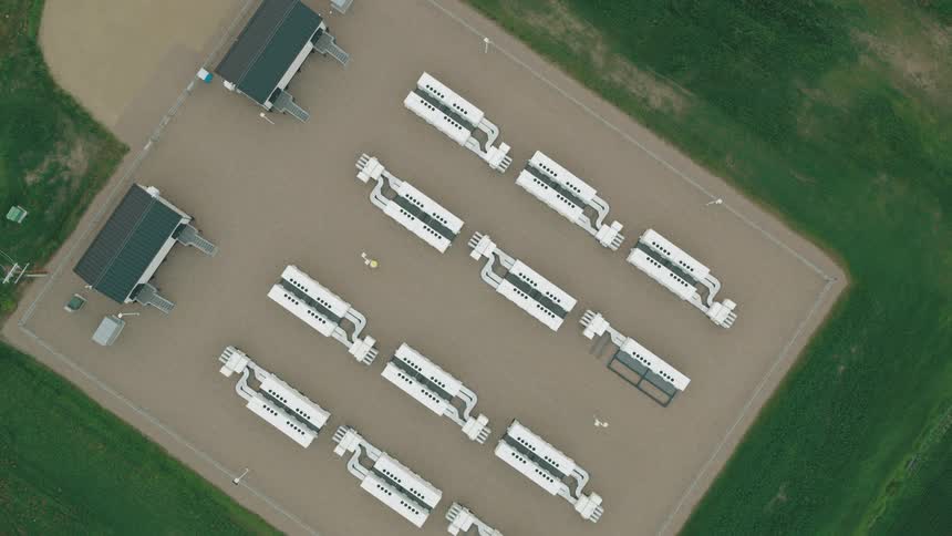 Aerial view of an industrial facility with rows of white battery cabinets surrounded by green fields