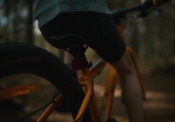 A young girl riding an orange bicycle through a forest path