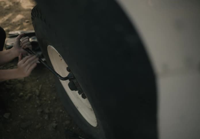 A person changing a tire on a vehicle using a lug wrench to tighten or loosen the lug nuts