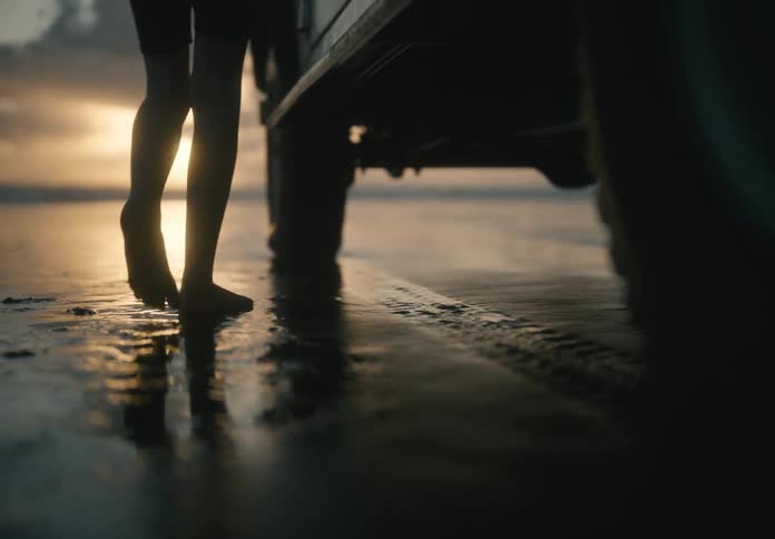 A child walks on a wet beach next to a vehicle