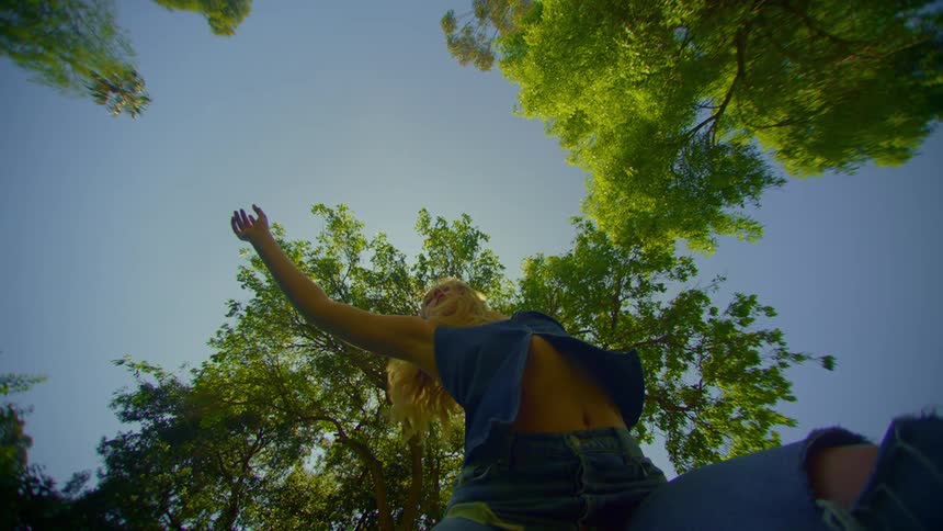 Blonde woman in jeans dancing in a place with trees