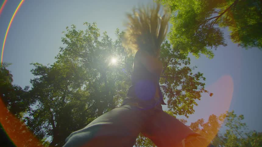 A lowangle view of a person dancing against a sunny sky with trees in the background