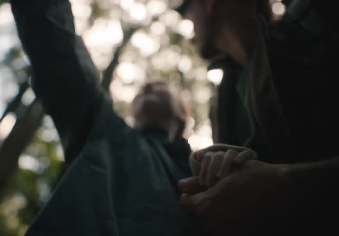 Two people holding hands viewed from below with a blurred background of trees and sunlight filtering through