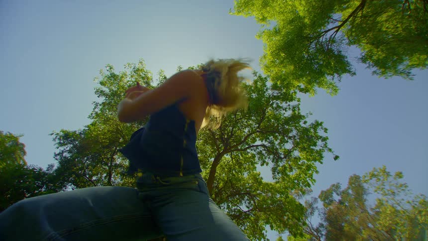 Upward view of a woman in jeans and a blue blouse dancing in a field with trees