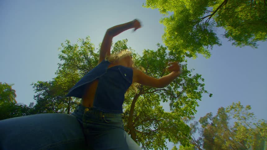A lowangle view of a person dancing against a sunny sky with trees in the background
