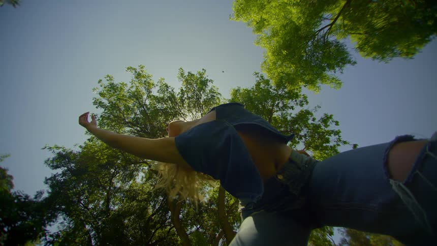 Blonde woman wearing jeans and a blue blouse dancing in a natural environment