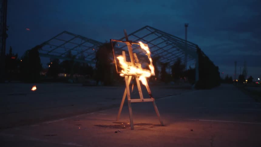 A now empty frame burning on an easel in a parking lot at dusk