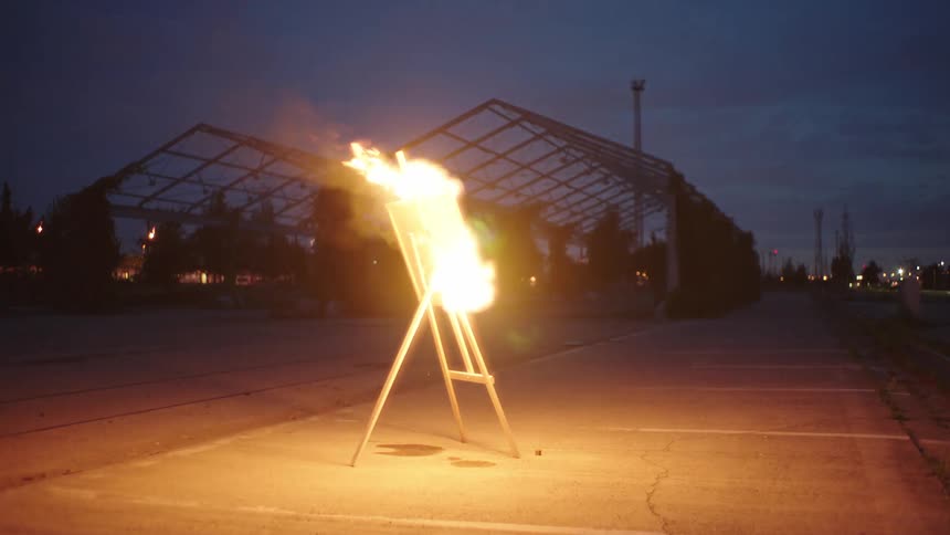 Painting fully aflame on an easel in the parking lot in the evening