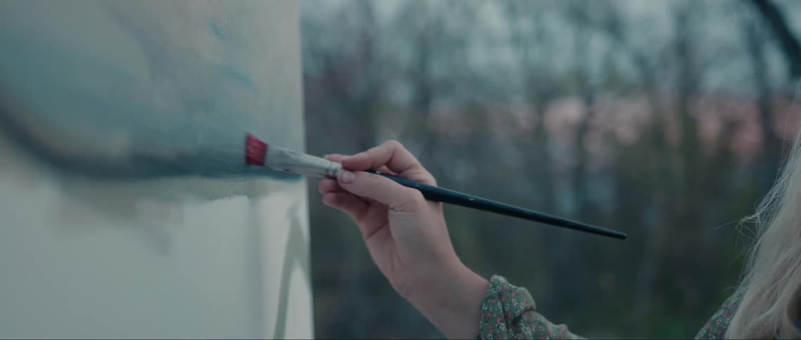 Woman hand holding a brush and painting a white canvas