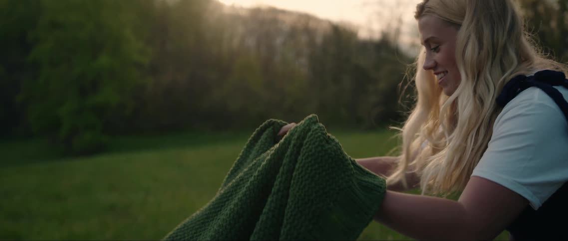 Woman placing a green towel in a field on the grass