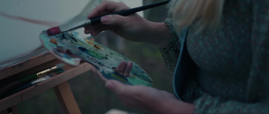 Hands of a painter with a palette and a brush painting a canvas