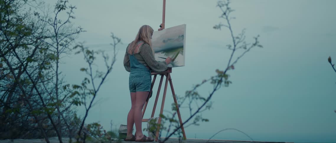 A woman is painting on a canvas outdoors set up on a tripod easel