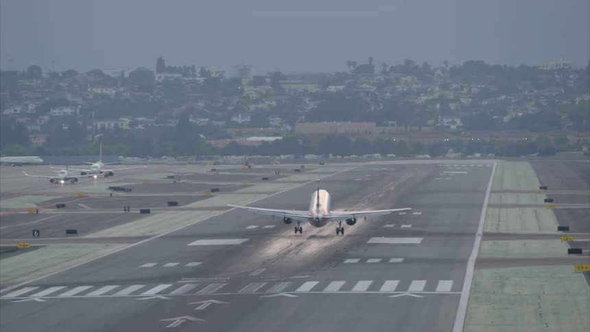 An airplane lands on the runway in front of a neighborhood on the hill