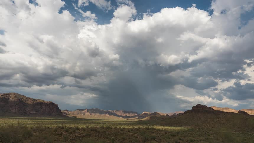 Timelapse footage captures distant rain falling from storm clouds over the desert landscape