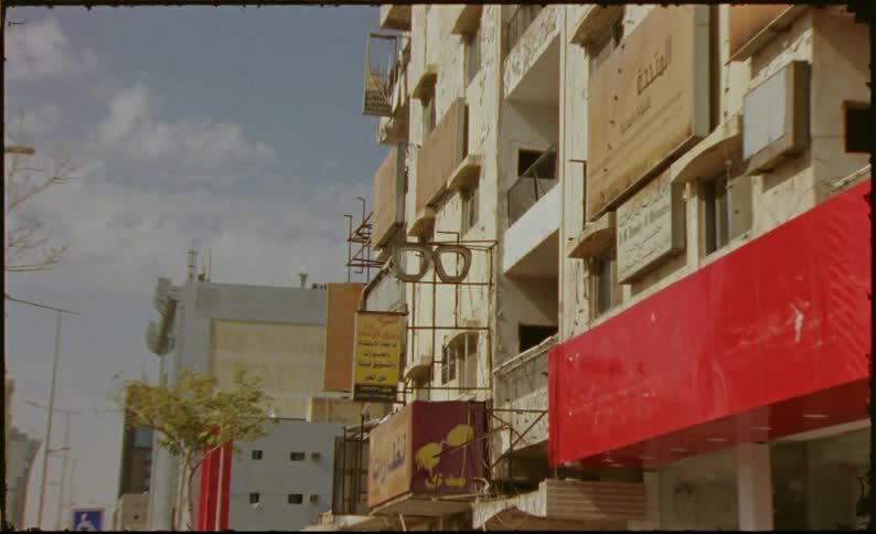 A store logo symbol in the shape of glasses is stuck to the wall of a building