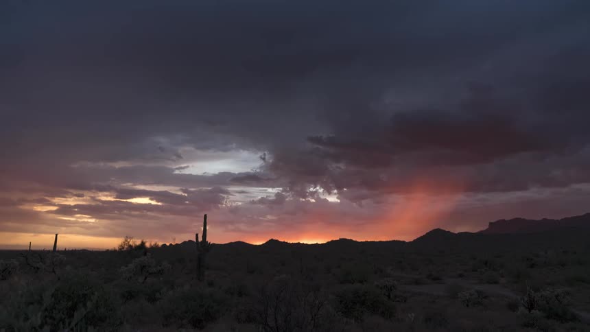 Sun sets turning mountains into silhouettes towering over an arid desert