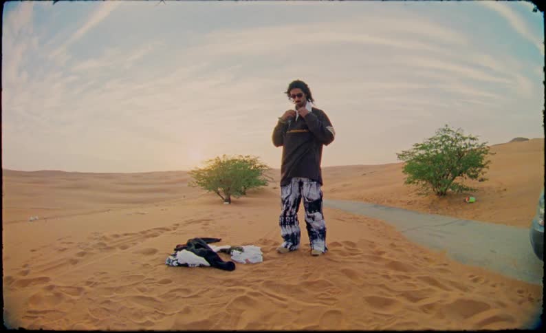 Man puts on a shirt and buttons it up in the desert