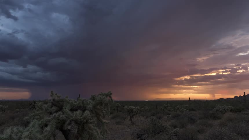 Timelapse footage captures distant rain falling from storm clouds over the desert landscape