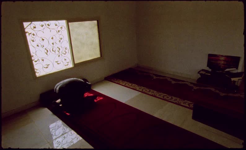 Man in a hoodie inside a room on his knees leaning his head on a rug as a religious sign