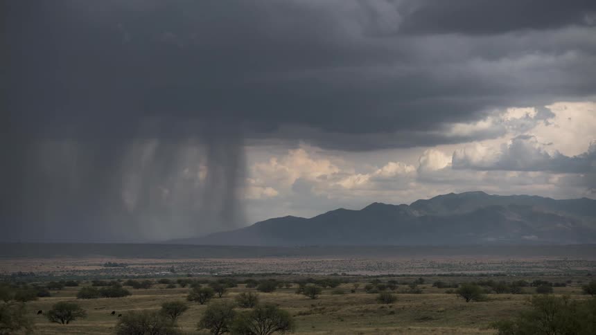 Landscape of a field with mountains in the background and a rain storm