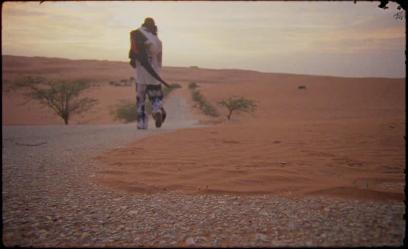 Person walking on foot on a narrow road surrounded by desert sands