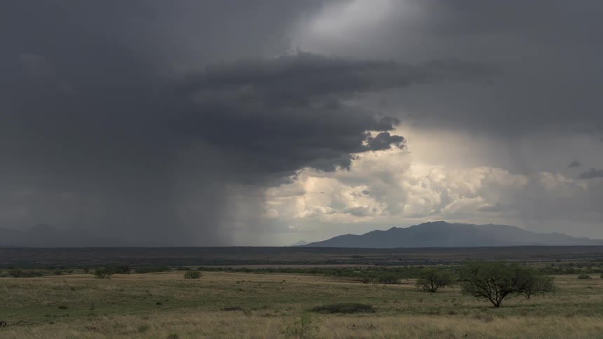 A rural region with mountains in the background and huge gray storm clouds in the sky