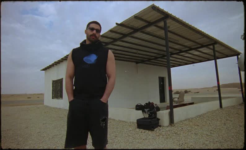 A man stands in front of his home in the desert