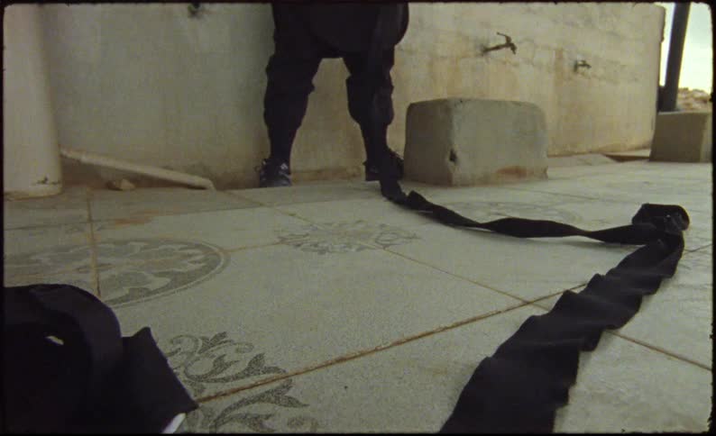 Person standing in the background next to a wall pulling a long black belt
