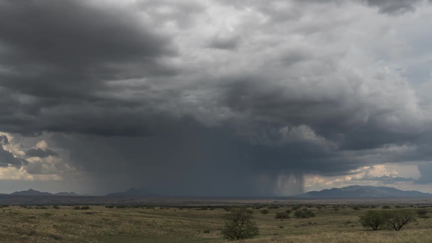Greenish field with mountains on the horizon of a rain storm