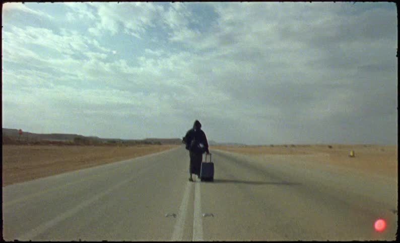 Man on a paved road walking with a suitcase