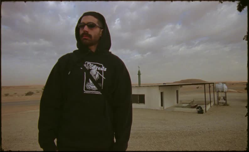 Man with sweatshirt and cap in a natural desert environment with a house in the background
