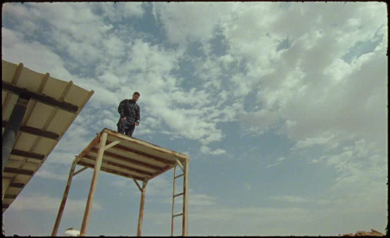 Man standing on a rusty platform wearing black clothing and punching the air
