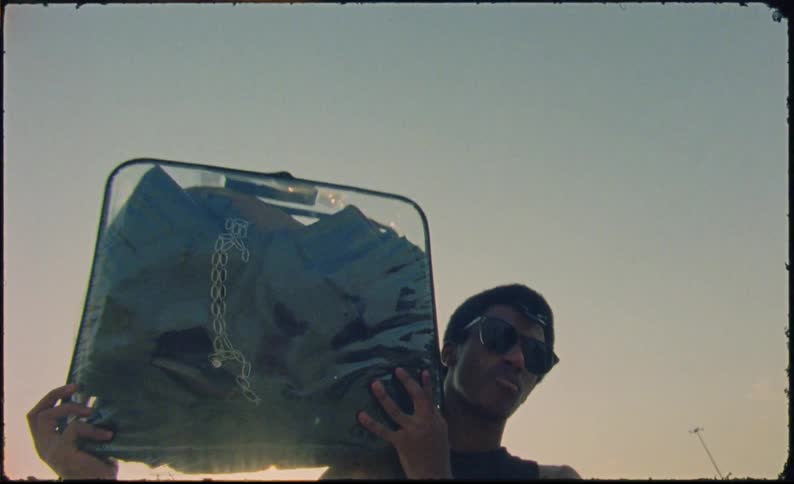 Man holds a clear suitcase on a beach at sunset