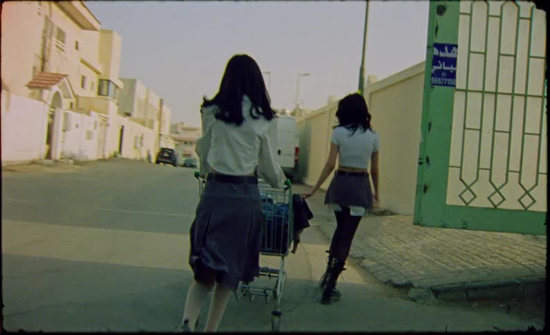Two girls wearing schoolgirl uniforms playing with a shopping entering an abandoned lot