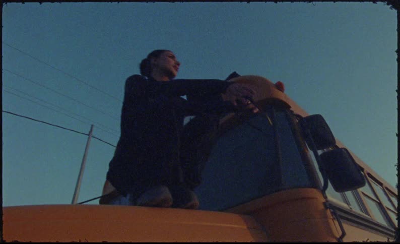 Woman on top of a bus on the hood sitting down