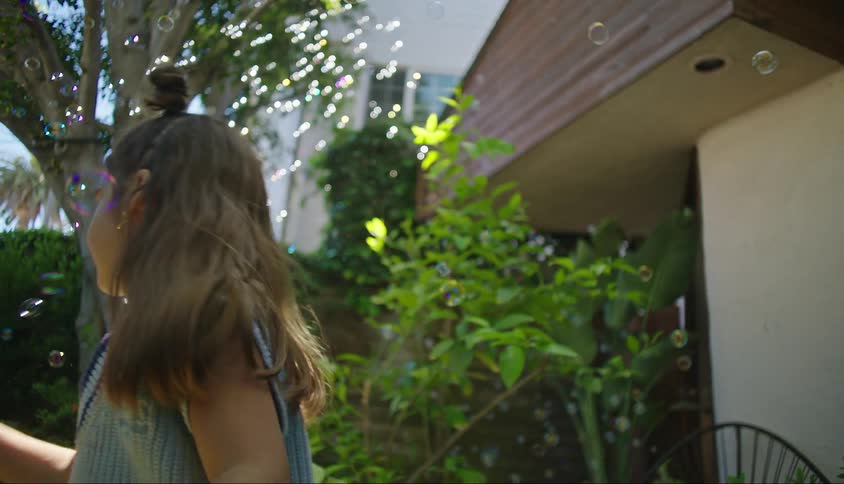 Portrait of a little girl in the backyard playing with soap bubbles that fly through the air