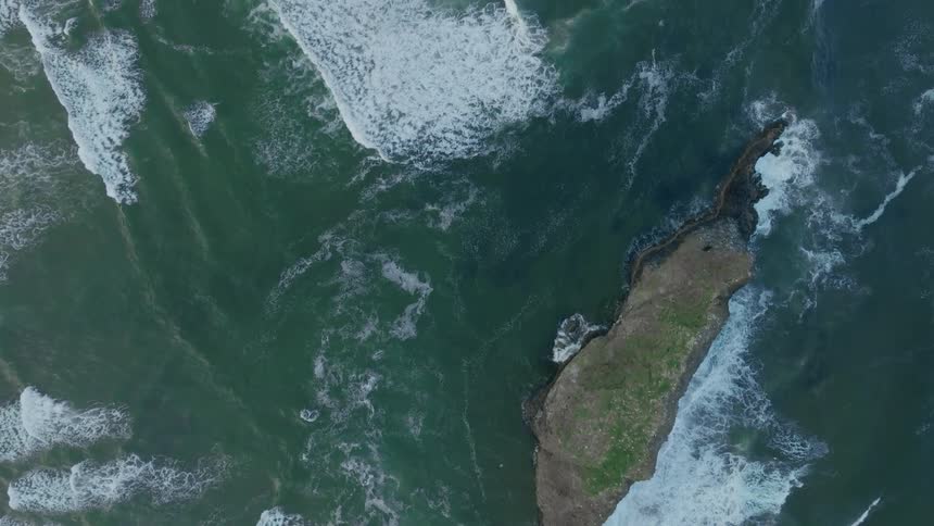 Aerial panorama of a rock in the middle of an ocean with strong waves