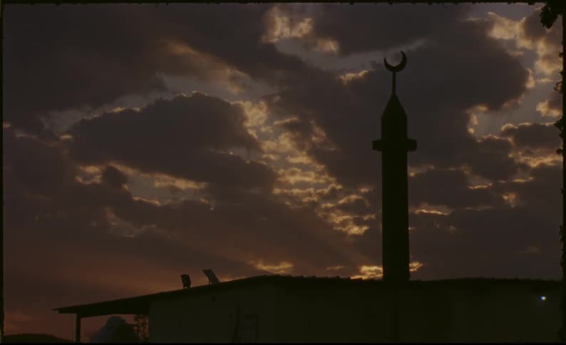 Silhouette of a house with a tower with a moon symbol at the top against a late afternoon sky with clouds