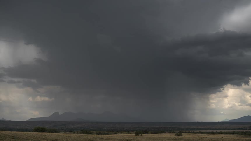 Storm with rain above a field with the silhouette of mountains on the horizon